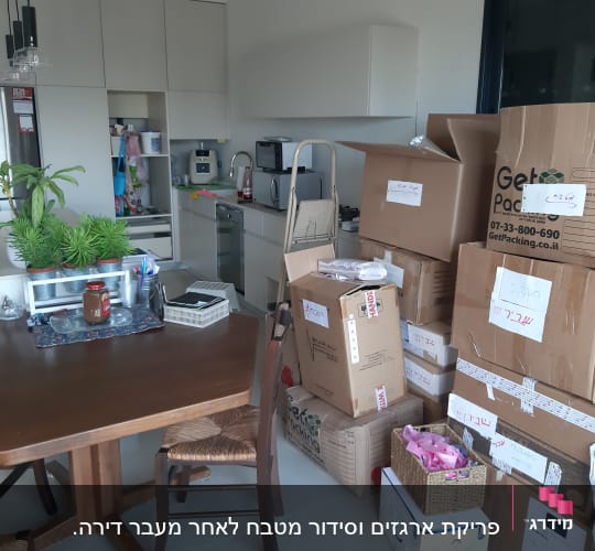 קופסאות קרטון מסודרות במטבח עם צמחים על השולחן